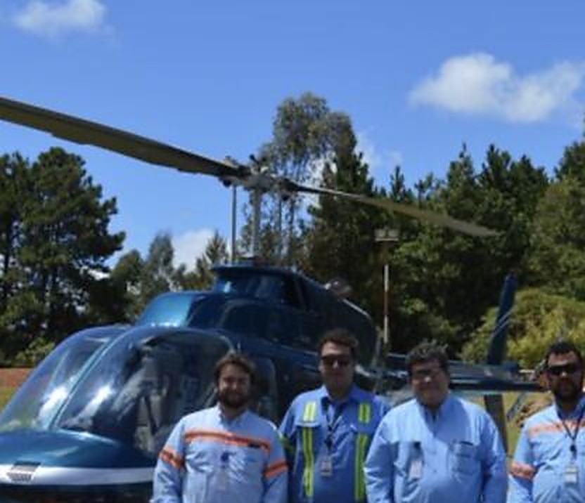 Equipe técnica em macacão e colete refletivo em frente a helicóptero